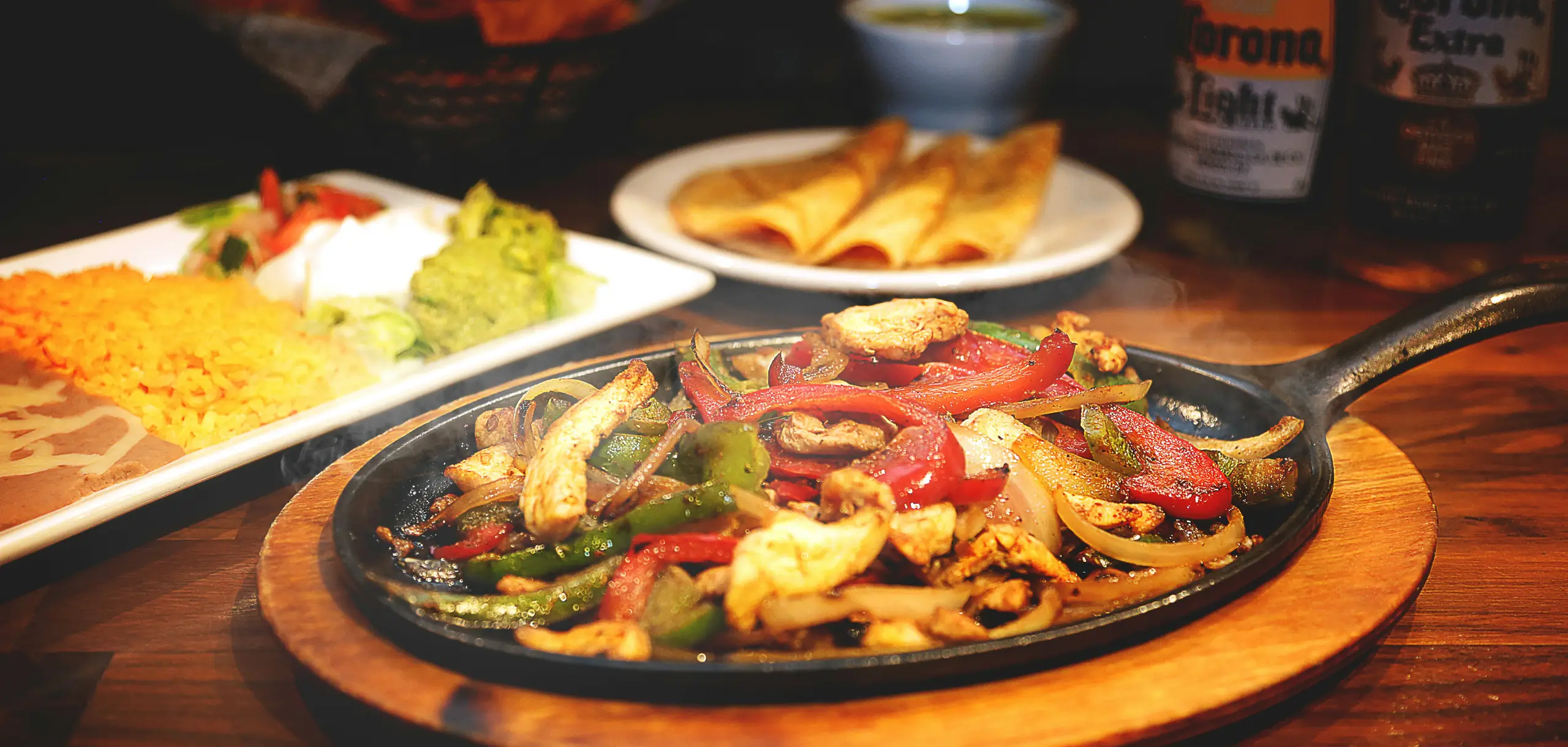Fajitas with peppers and onions sizzling on a cast iron skillet, served with rice, guacamole and chips