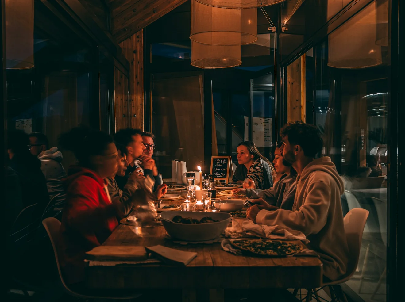 Guests sharing a meal together around a long table in a warmly lit restaurant