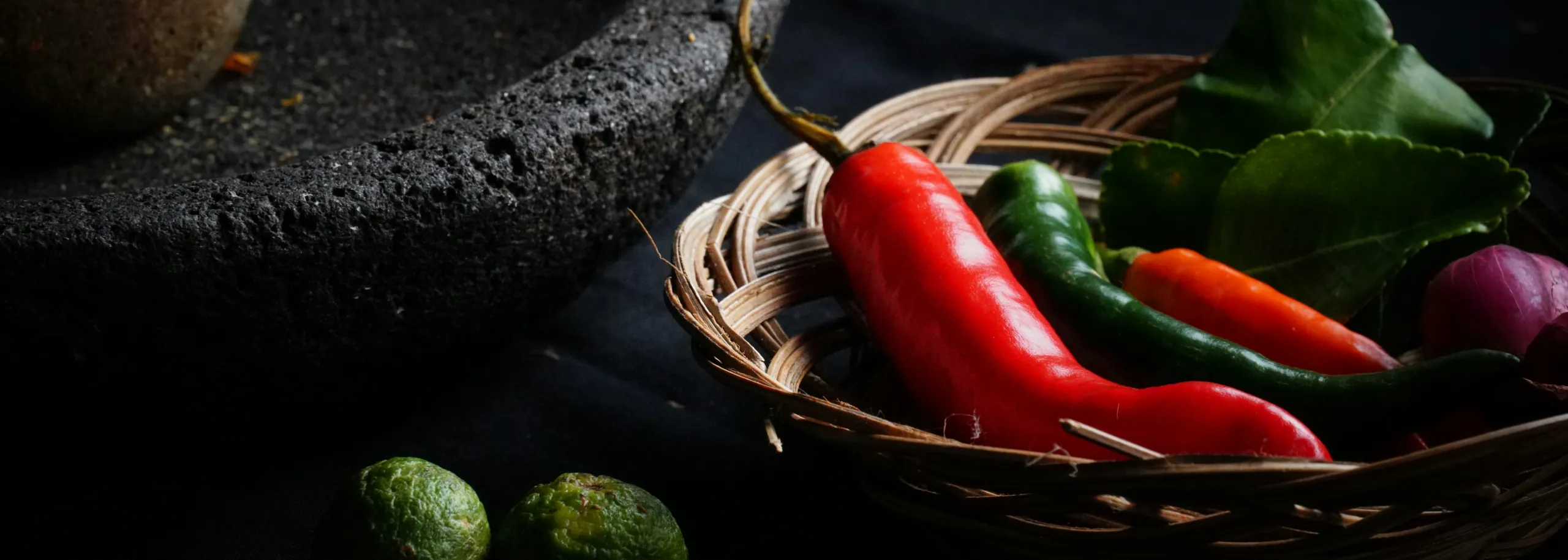 Fresh chiles and limes beside a stone molcajete