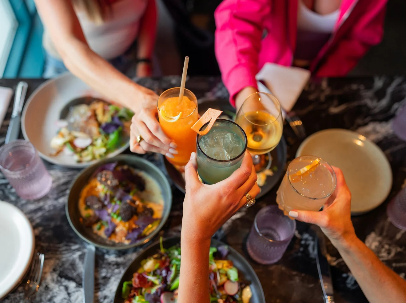 Friends raising drinks together over a table of shared plates