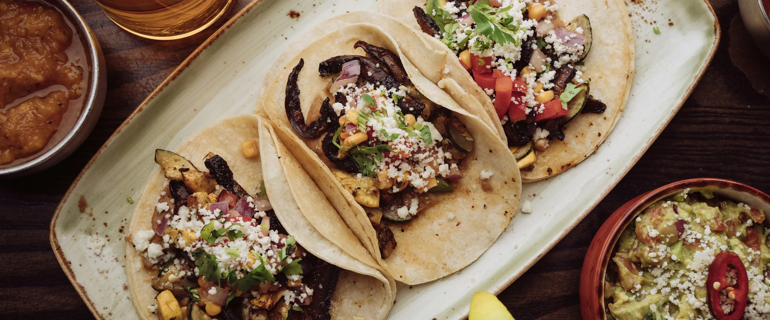 A shared platter of tacos with guacamole and salsas on a rustic wooden table