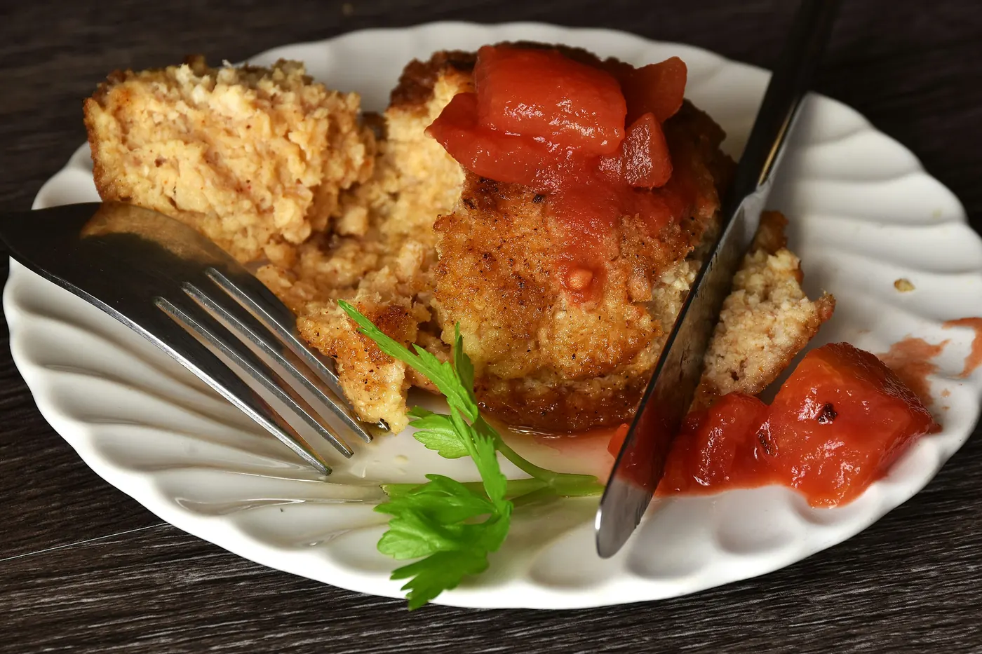 A battered fried item on a white plate with red sauce beside it
