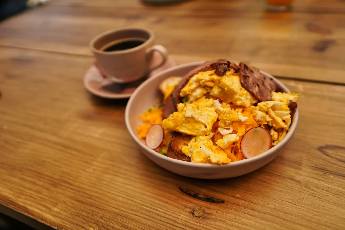 A bowl of sauced tortilla pieces beside a cup of coffee on a wooden table