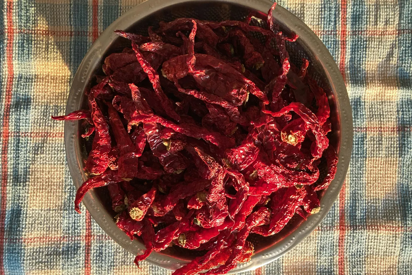 A metal bowl of dried red chiles resting on a checked cloth