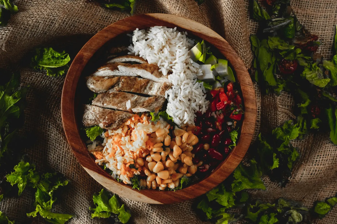 An overhead bowl of grilled chicken with rice, beans and fresh greens