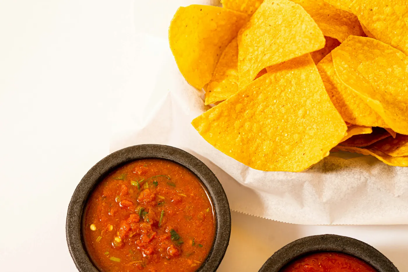A bowl of red salsa beside a basket of tortilla chips