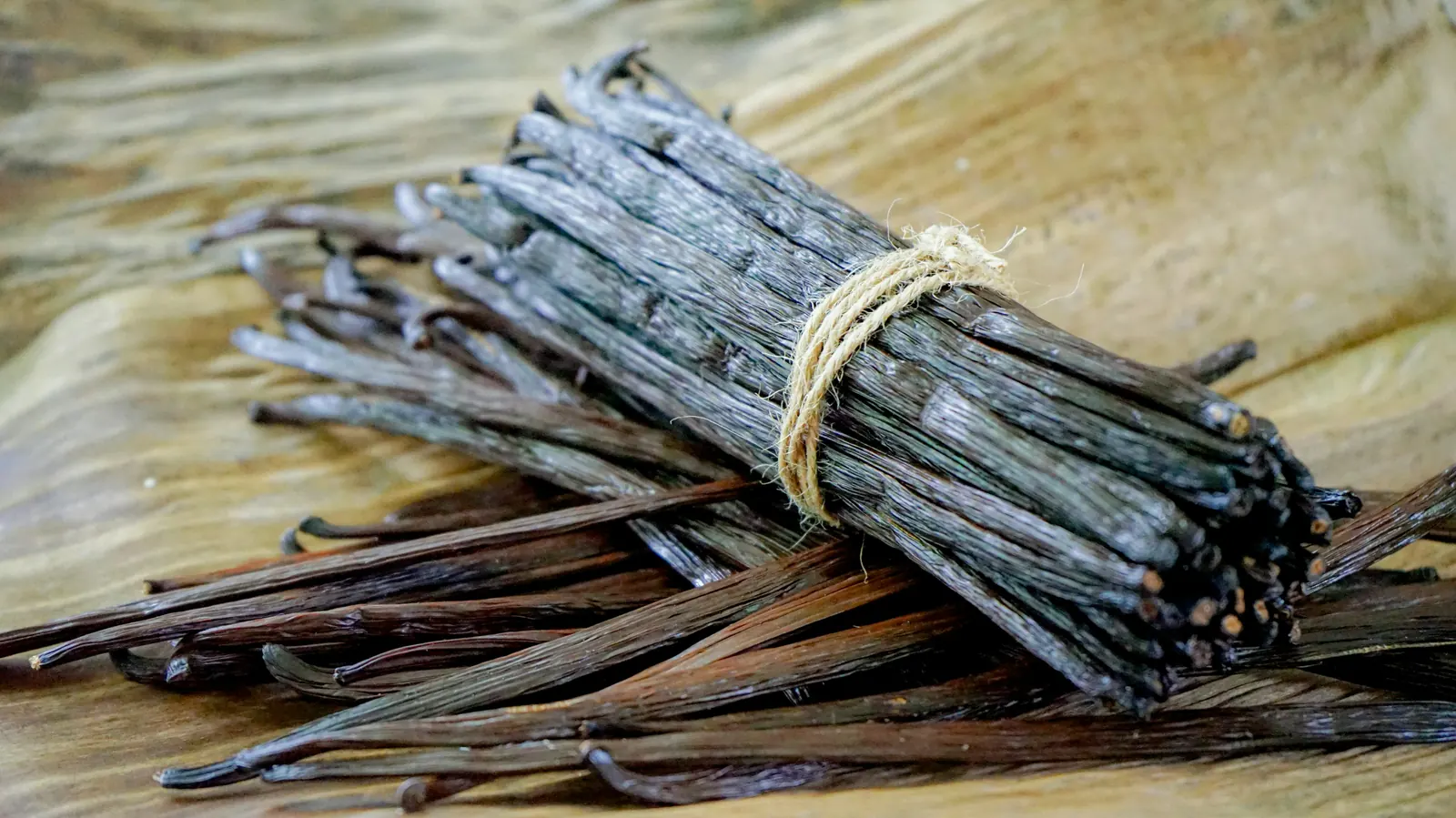 A bundle of dark cured vanilla beans tied with string on a wooden surface