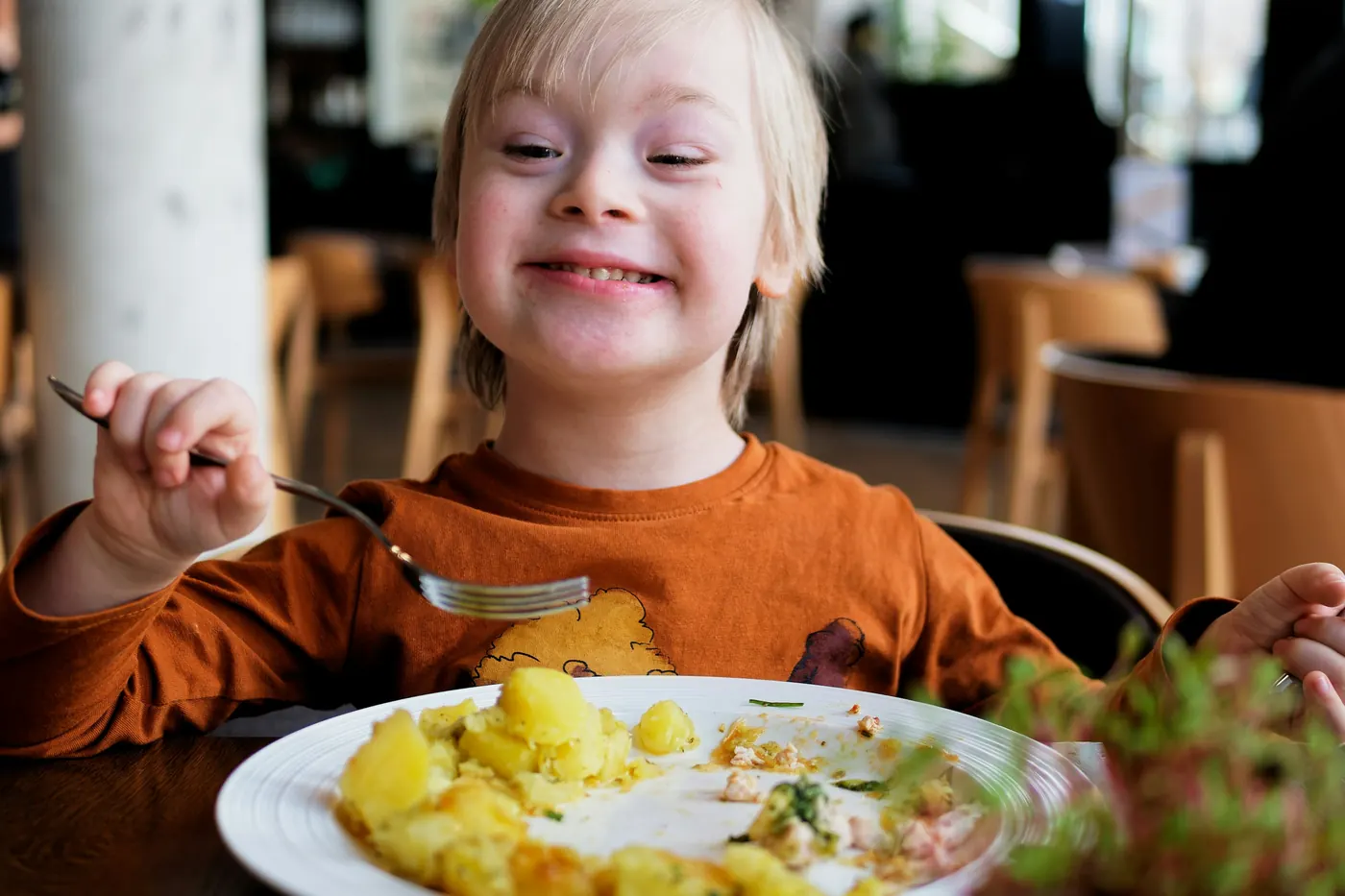 A smiling child eating from a plate with a fork