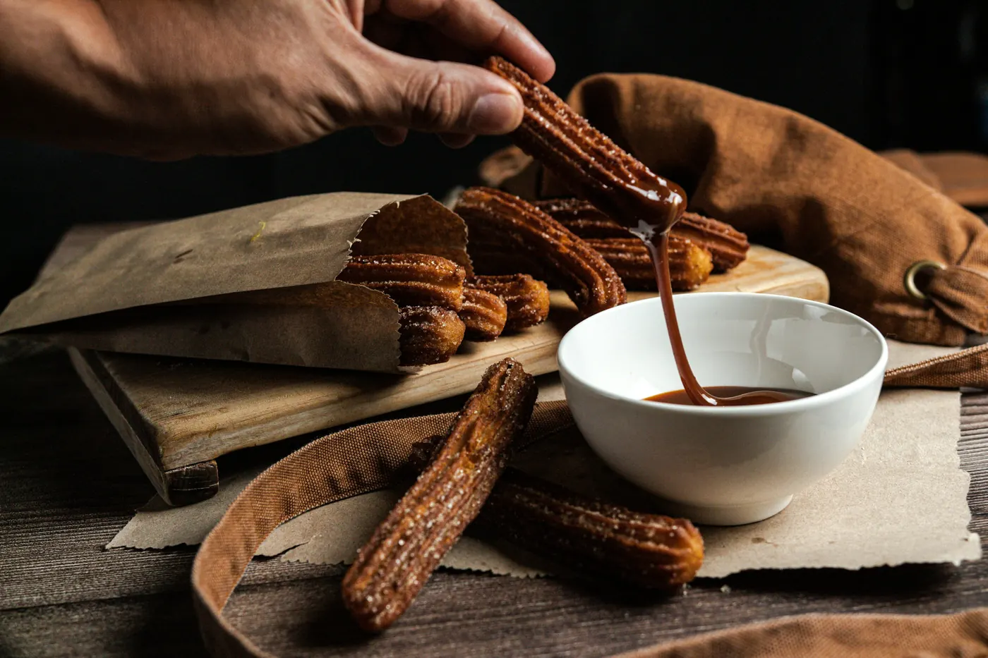 A churro being dipped into a bowl of dark chocolate