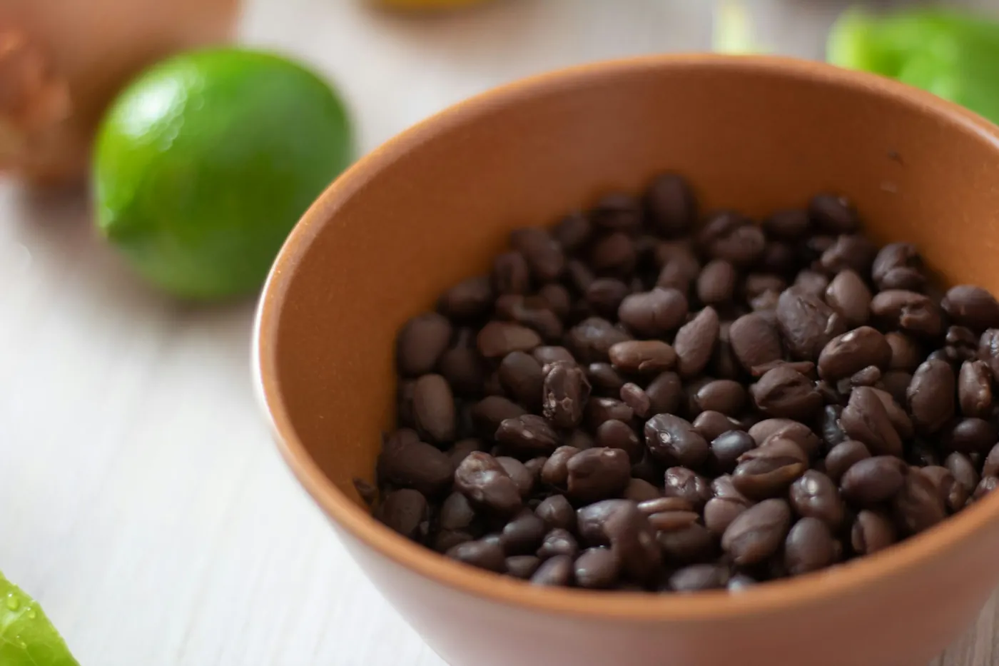 A clay bowl of cooked black beans with a fresh lime alongside