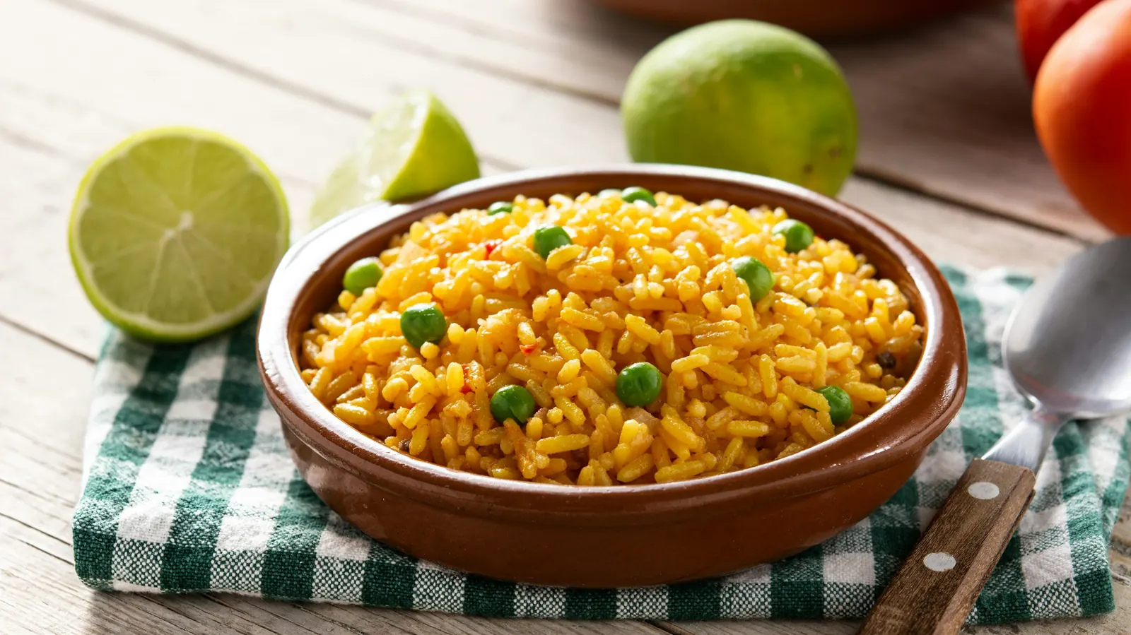 A clay bowl of orange-red seasoned rice with a lime alongside