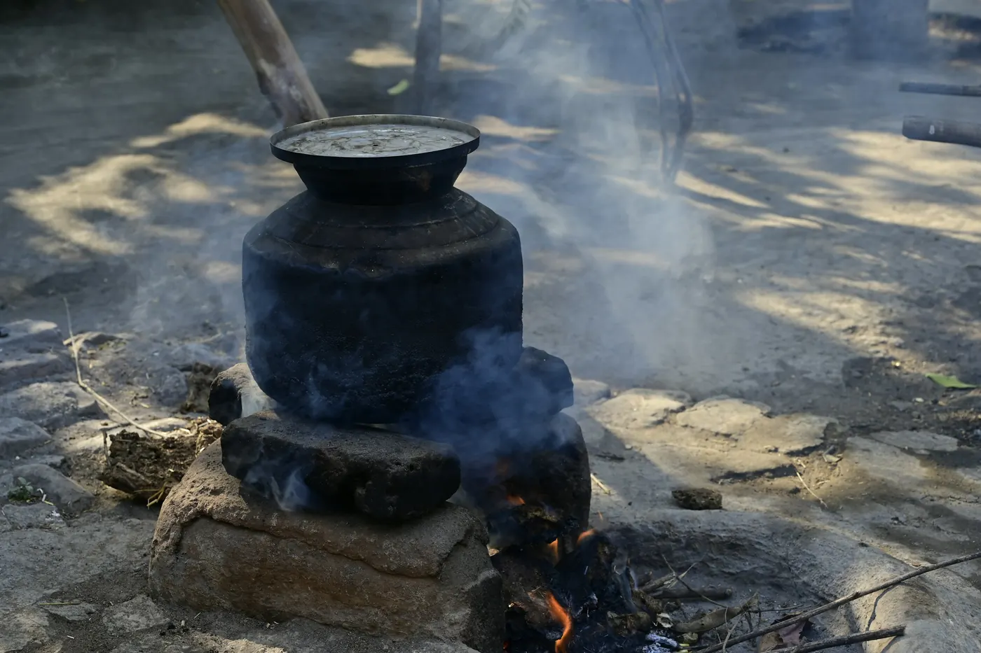 A clay pot sitting over a smoking wood fire