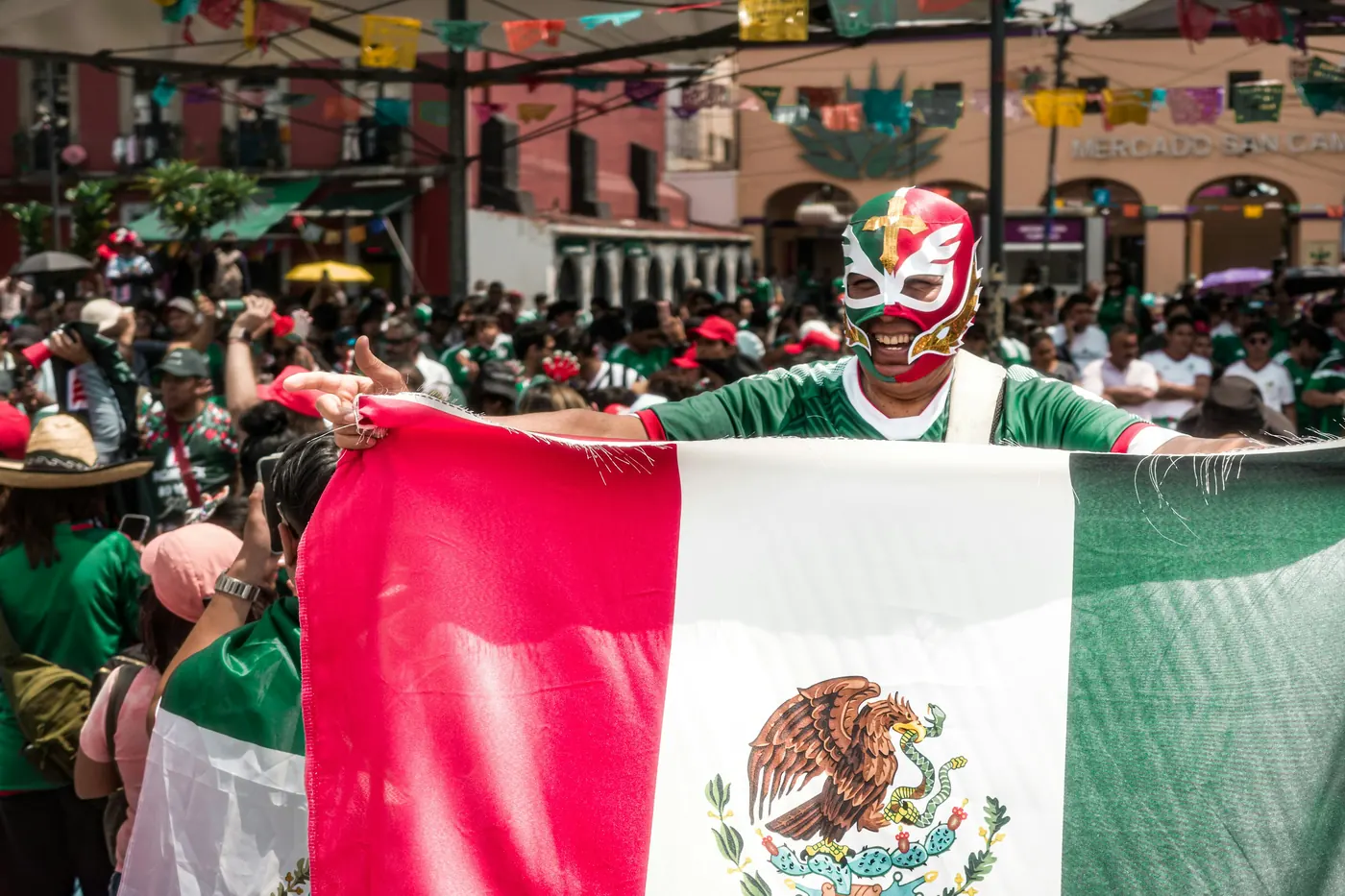 A crowd in a street holding up a large national flag