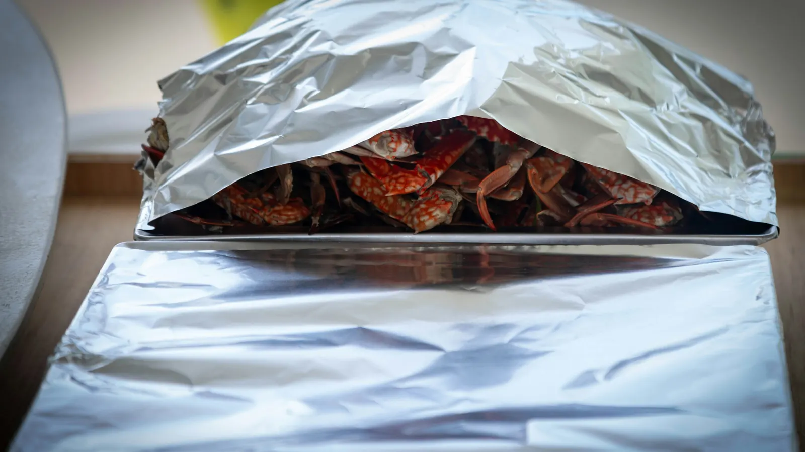 A foil-covered tray being opened to reveal the food inside