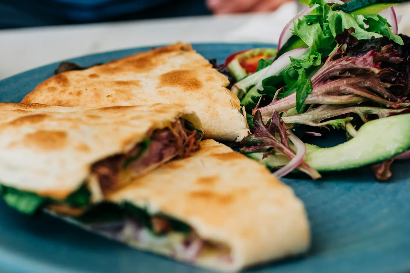 A folded quesadilla served on a blue plate with salad