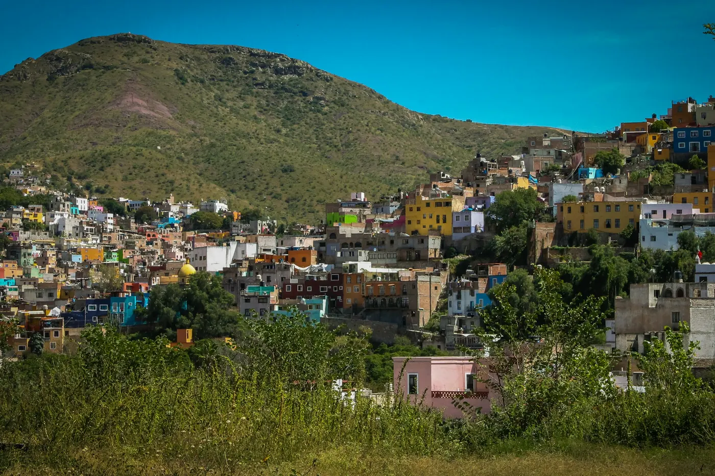 A dense hillside town of low colored houses below a rocky peak