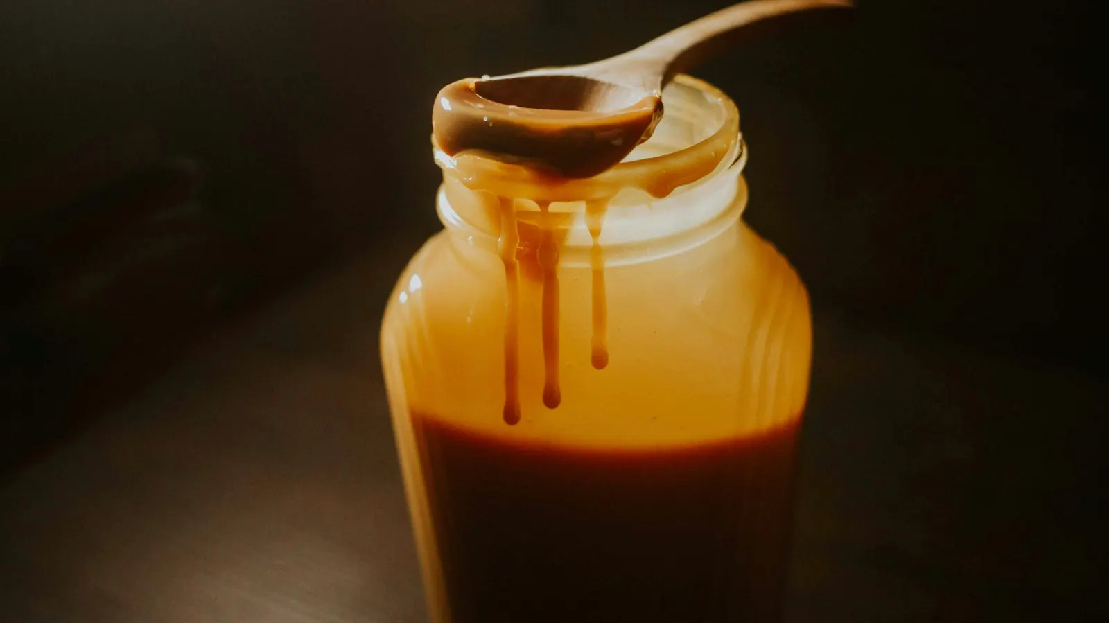 A glass jar of thick amber caramel with the sauce running down the side