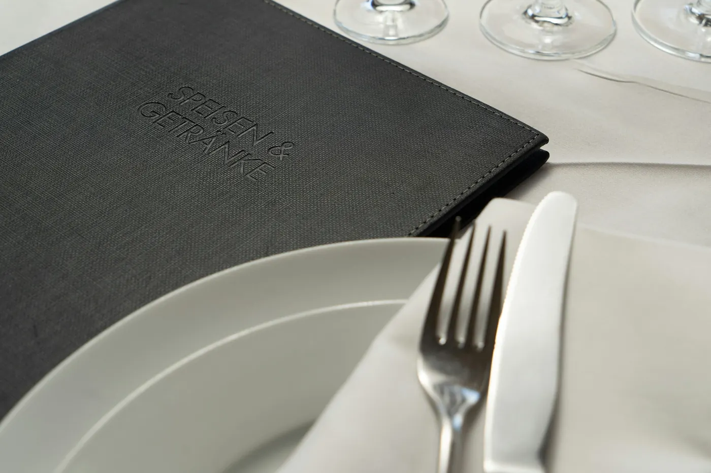 A closed menu folder next to a plate, fork and knife