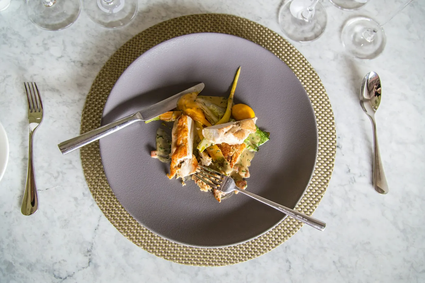 A small serving of food on a plate set over a larger charger
