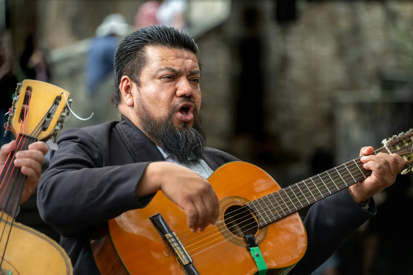 A musician in dark dress playing an acoustic guitar outdoors