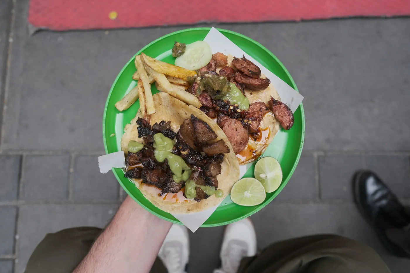 A hand holding a paper plate of tacos with lime wedges