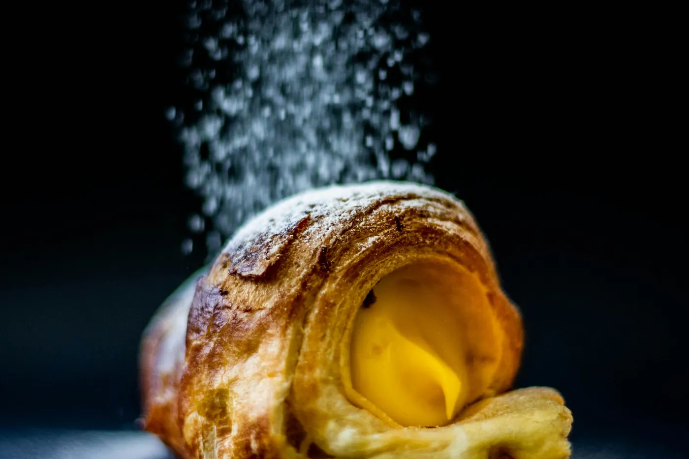 A dusted pastry broken open to show pale custard inside