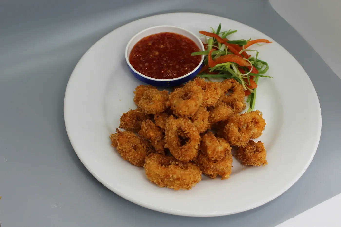 A white plate of breaded fried shrimp with a dipping sauce