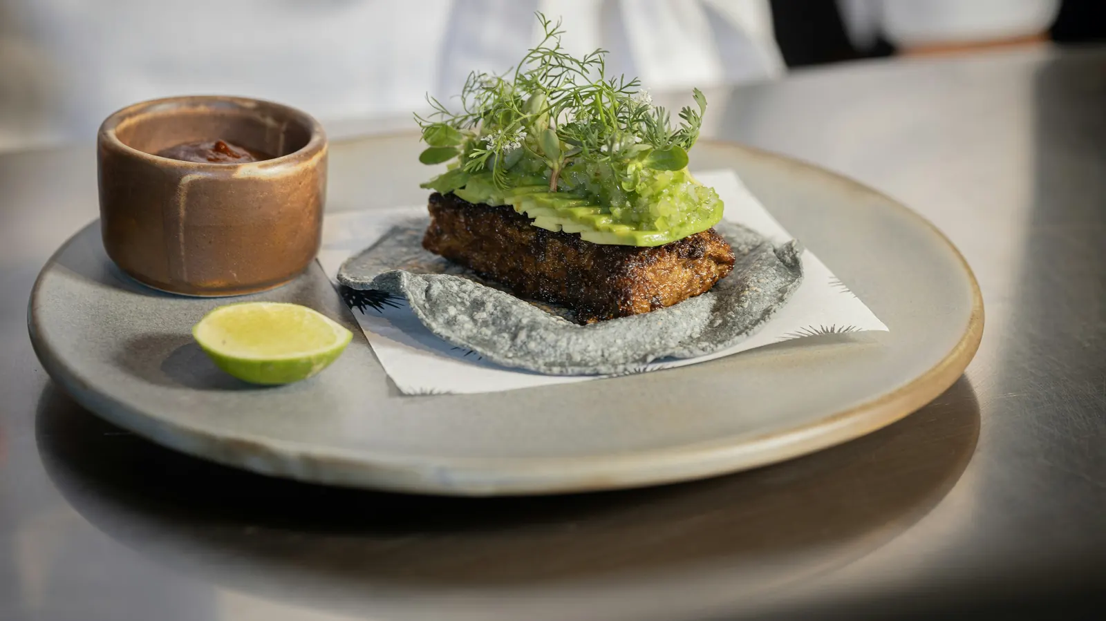 A plated fish fillet topped with avocado and served with lime