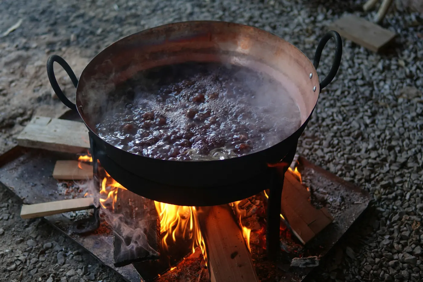 A dark pot of beans simmering over an open fire