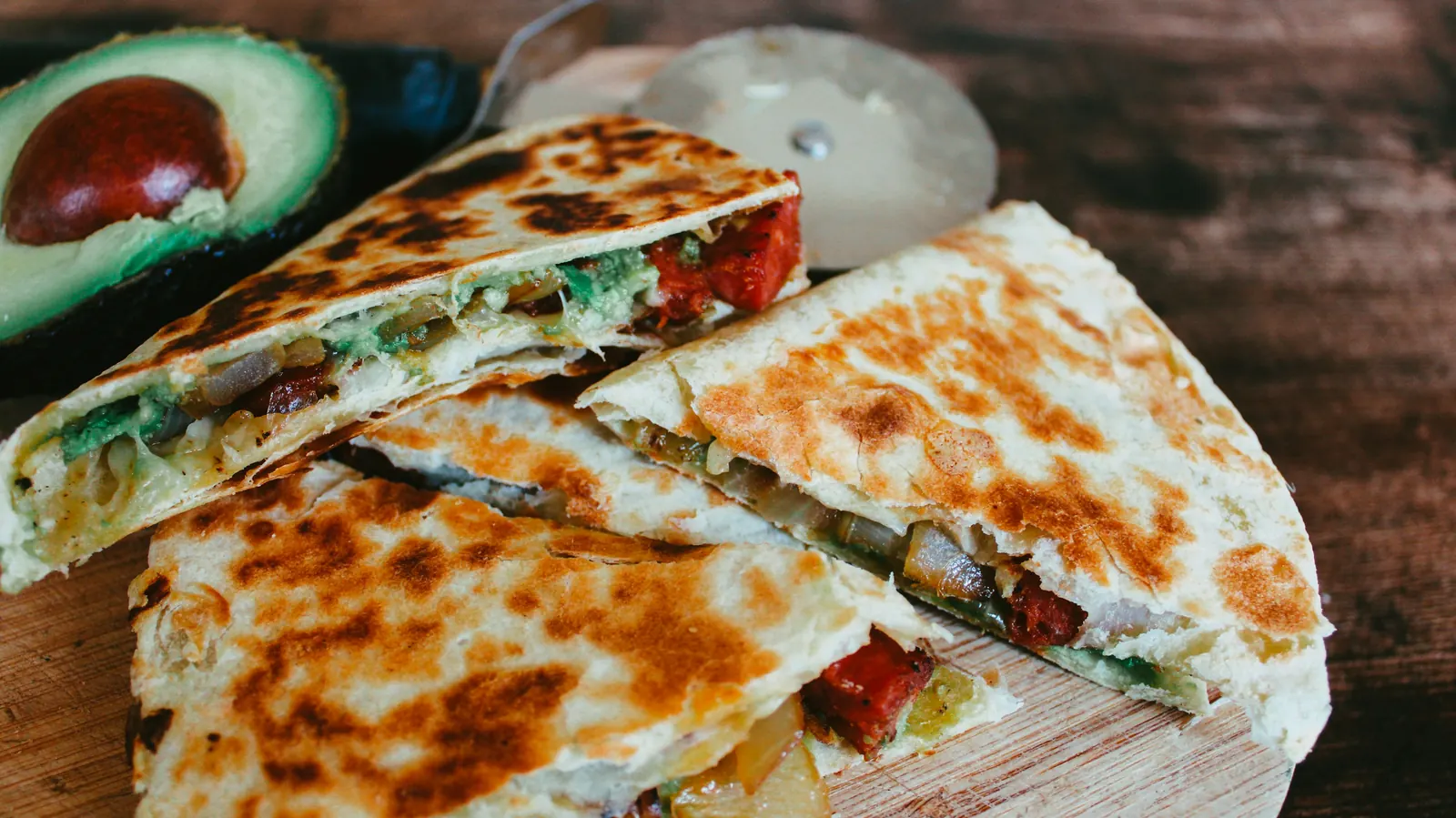 A quesadilla cut into wedges on a board with avocado and tomato