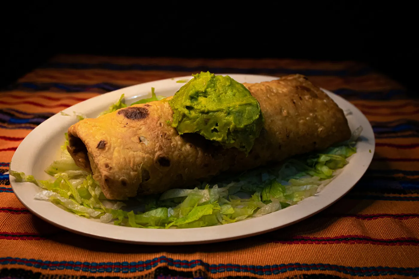 One large rolled and fried tortilla on a plate with lettuce