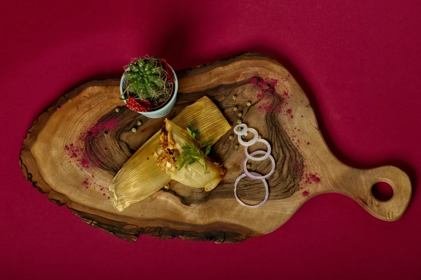 A single tamal plated on a wooden board with a small garnish