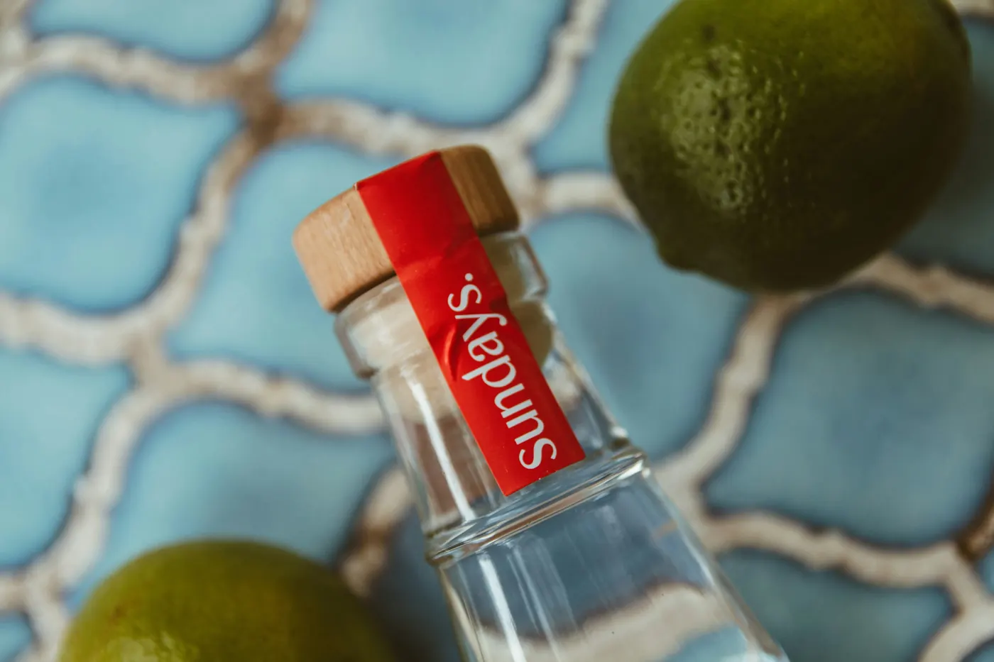 A small glass bottle lying on tiles beside a cut lime