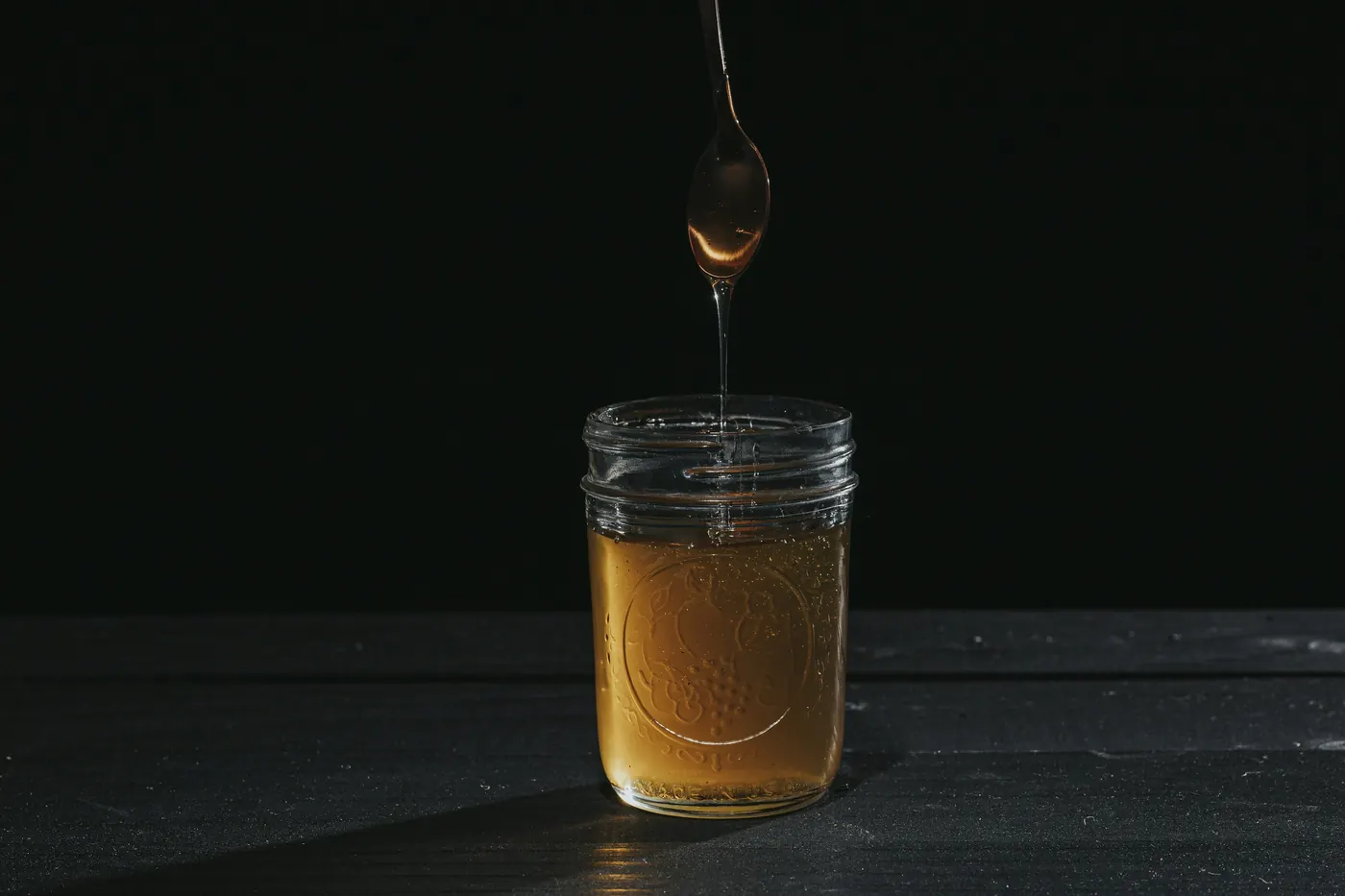 A small jar of amber sauce with a spoon lifting from it against a dark background