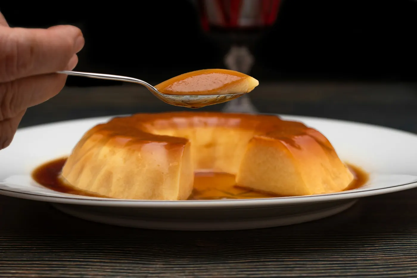 A spoon lifting a piece from a whole flan on a plate
