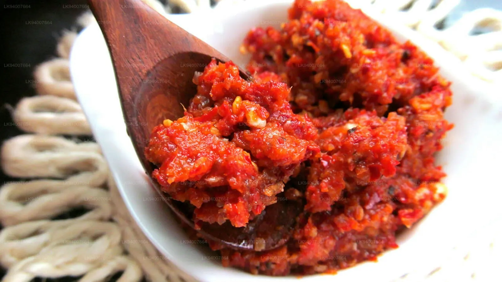 A wooden spoon lifting a deep red seasoning paste from a bowl