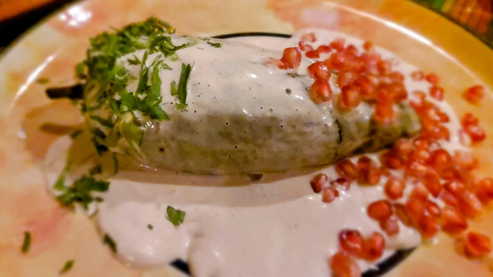 A stuffed green pepper under a white sauce scattered with pomegranate seeds
