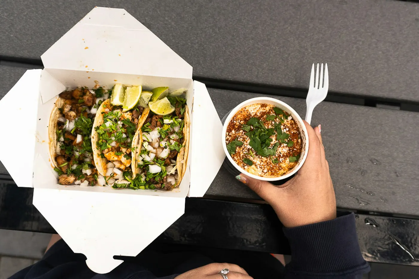 An overhead view of a takeout box holding tacos and a small bowl