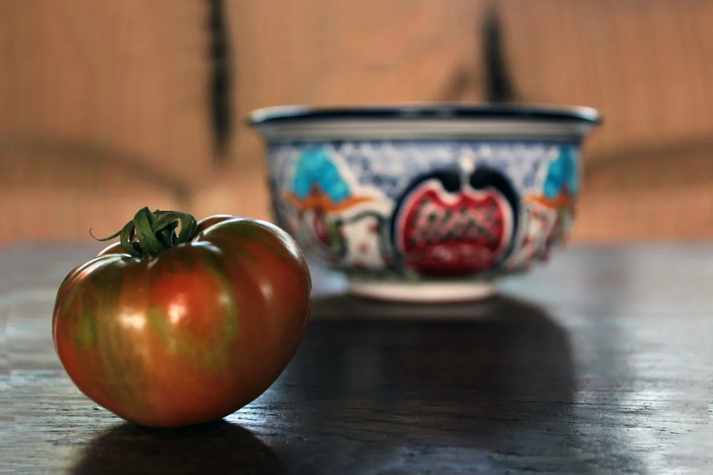 A ripe tomato on a dark surface beside a patterned bowl
