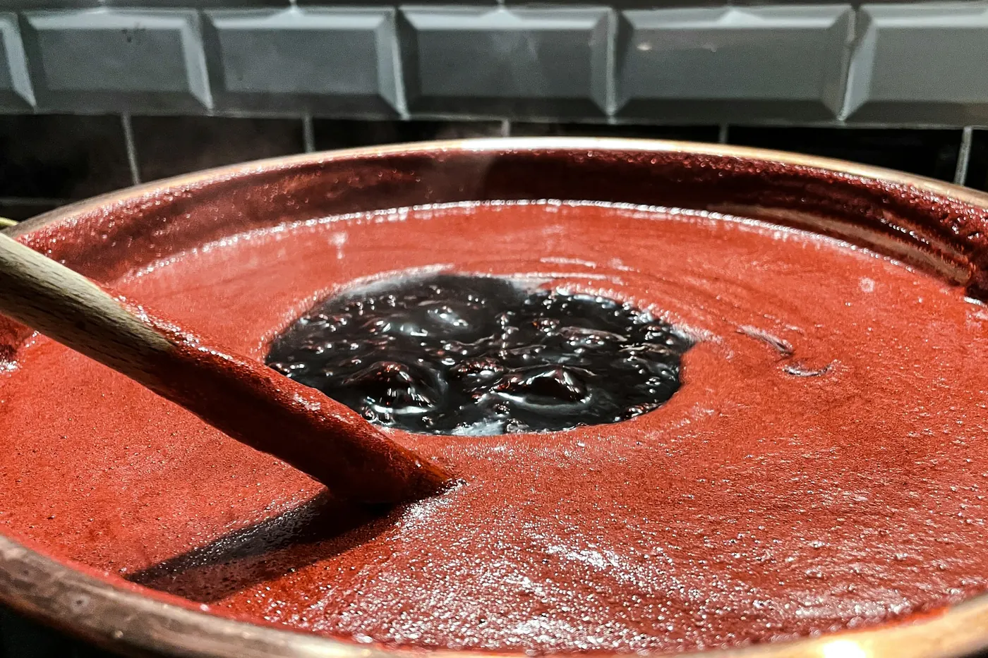 A wide shallow pan of deep red sauce with a spoon resting in it