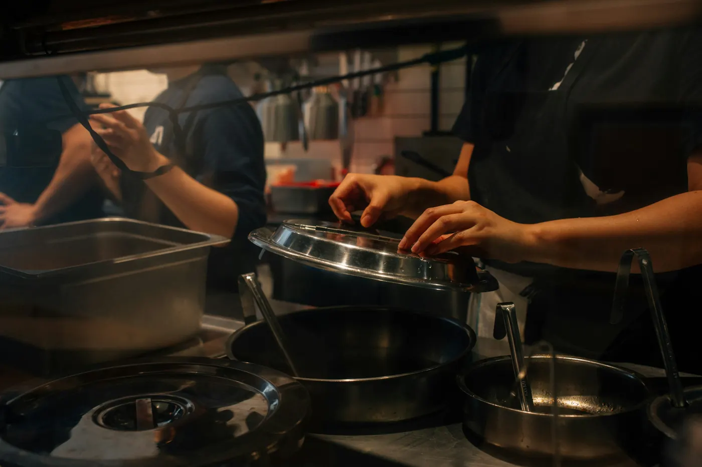 Hands working over steel pans on a busy kitchen line