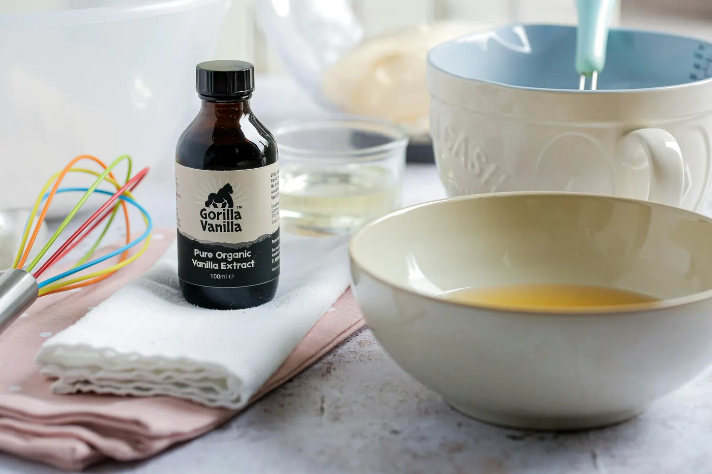 A small dark bottle of extract beside mixing bowls and a whisk