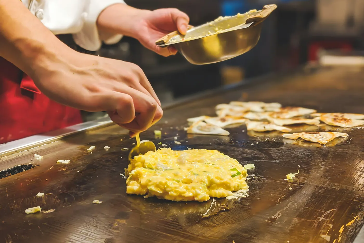 Hands assembling filled tortillas on a large hot griddle