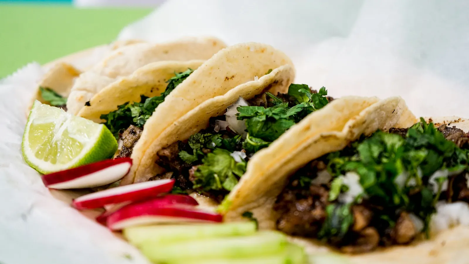 Corn tortilla tacos filled with shredded beef, served with lime and radish