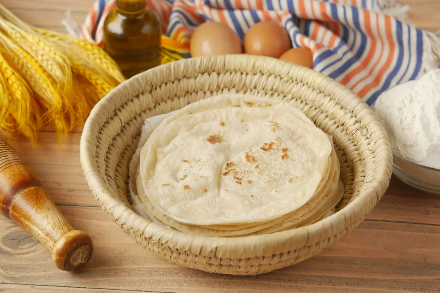 A woven basket of soft flour tortillas beside fresh corn and eggs