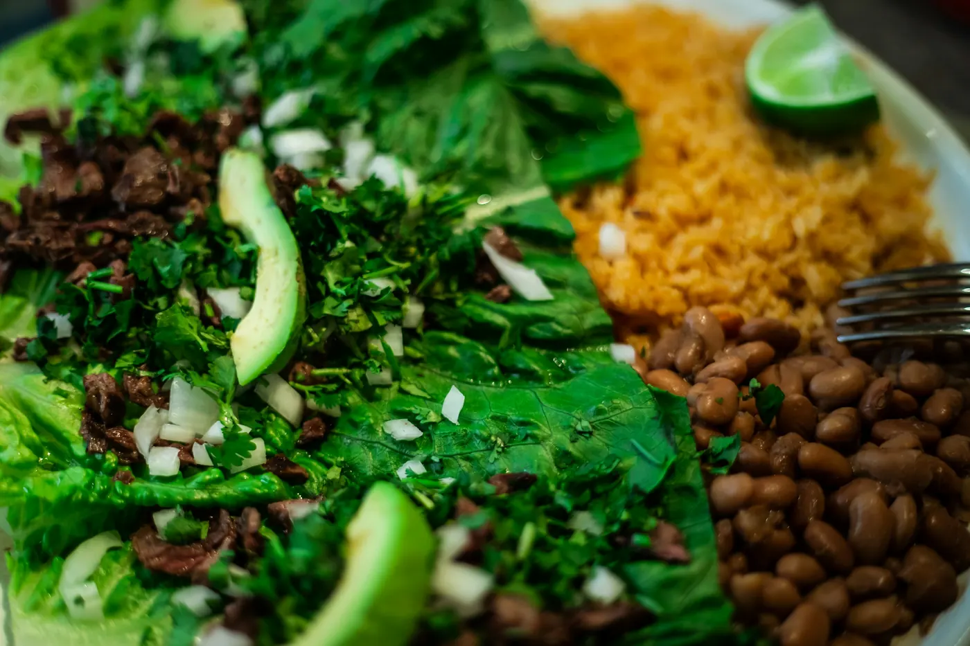 A bowl of beans and rice with fresh green vegetables and avocado