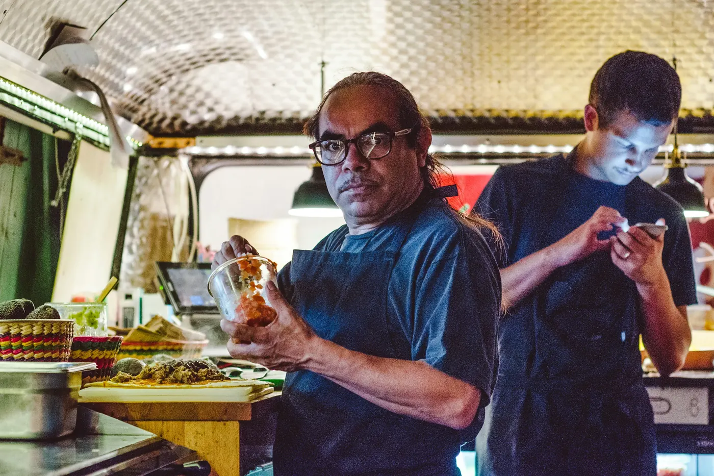 Two people at a food truck window with prepared food in the foreground