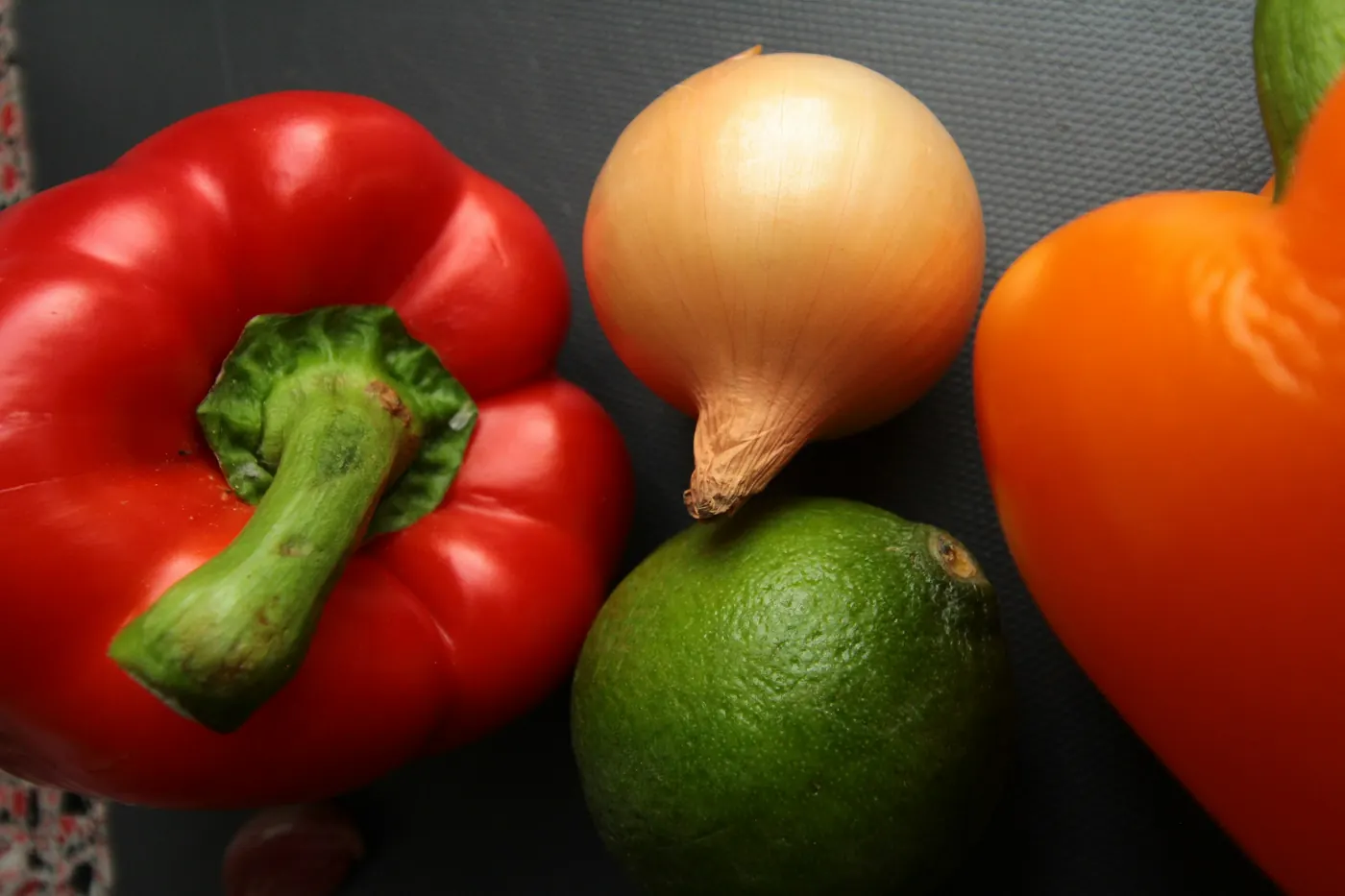 Red and orange bell peppers, a white onion and a fresh lime