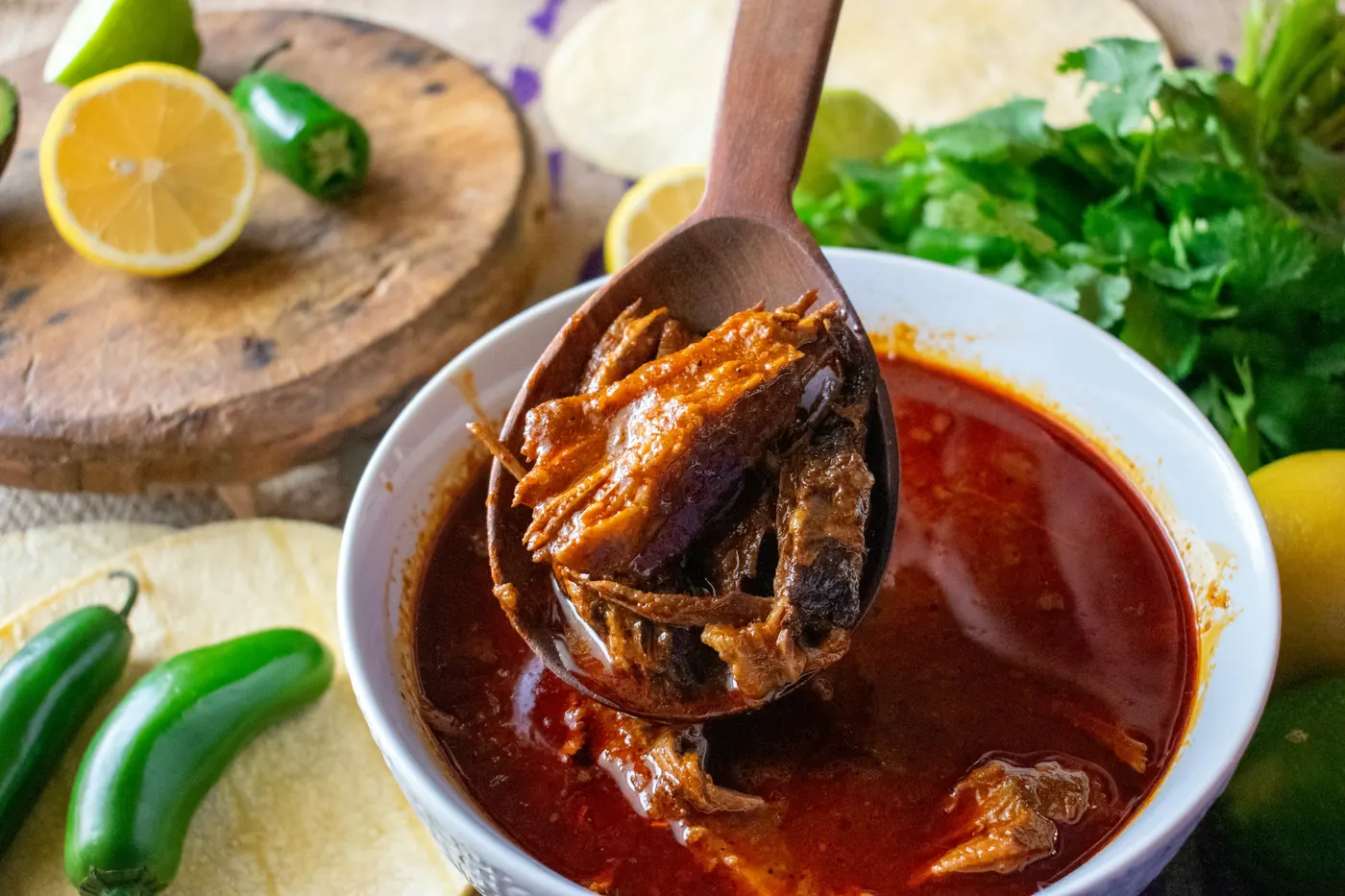 A spoon lifting shredded beef from a bowl of deep red birria broth
