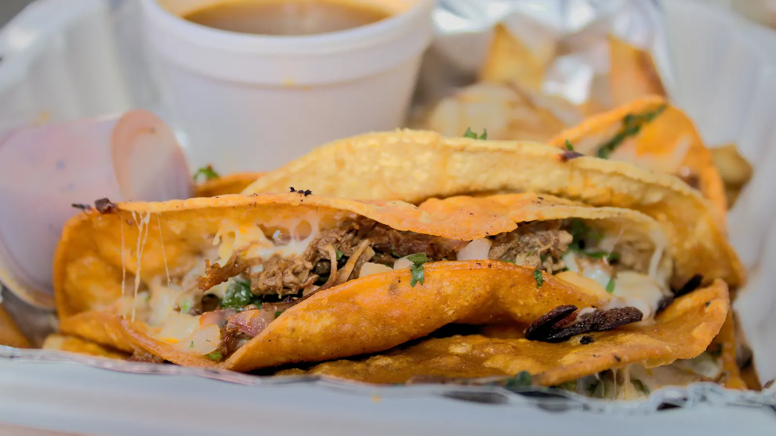 Crisp folded birria tacos served beside a cup of red consome